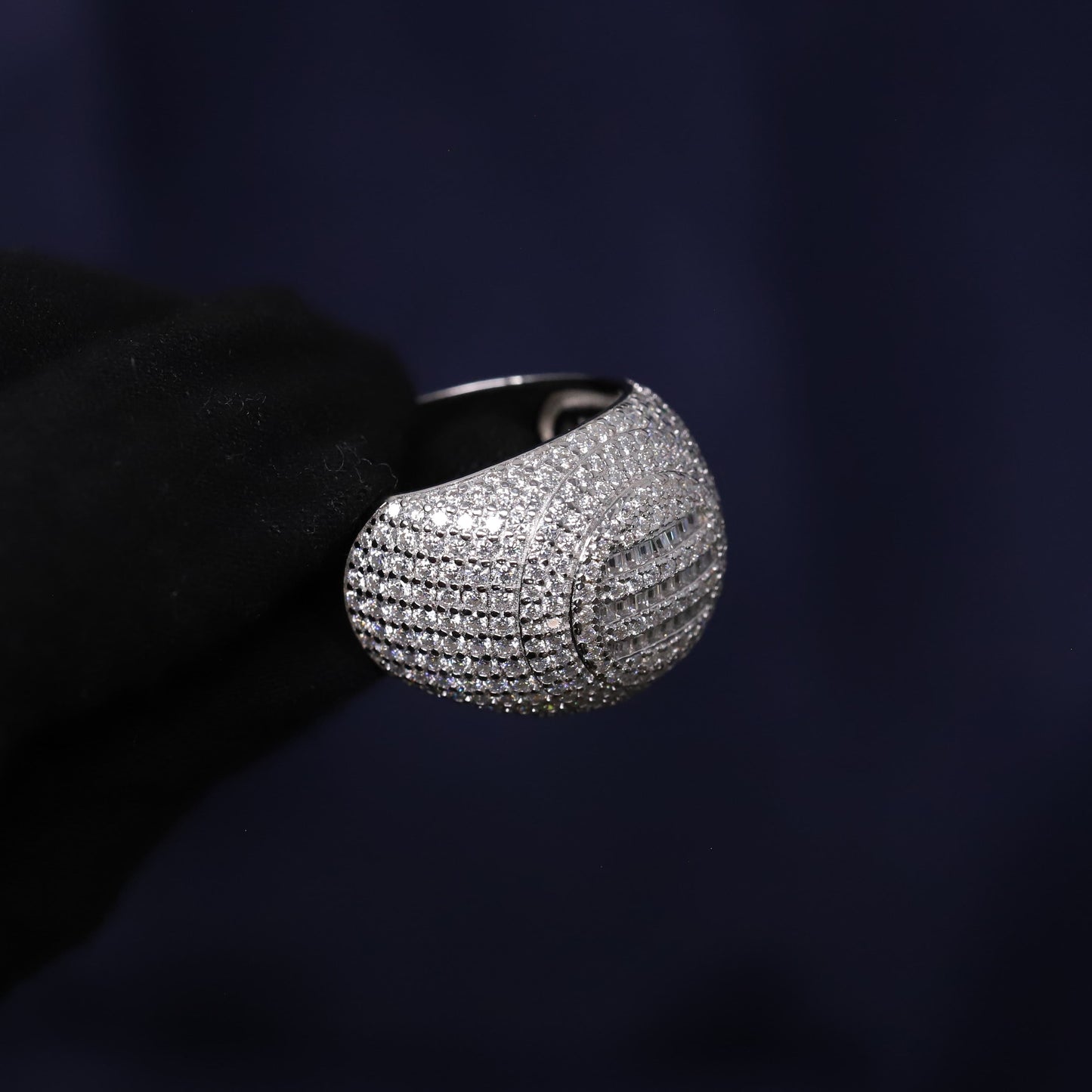 Silver ring with gemstones held by a black gloved hand against a dark background