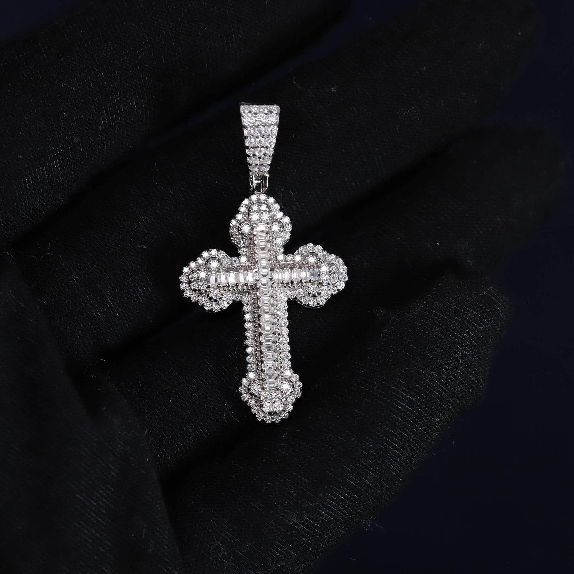 Silver cross pendant with clear stones on a black fabric background