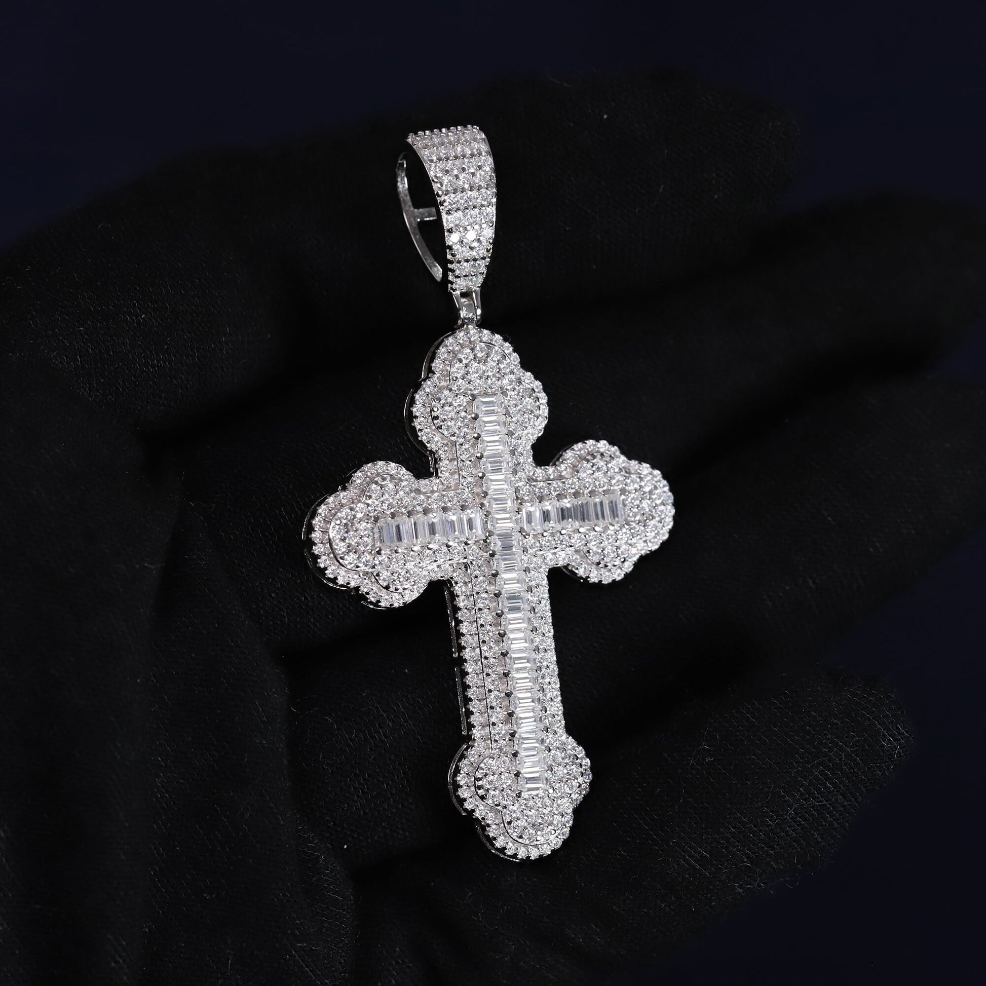 Silver cross pendant with clear stones on a black background