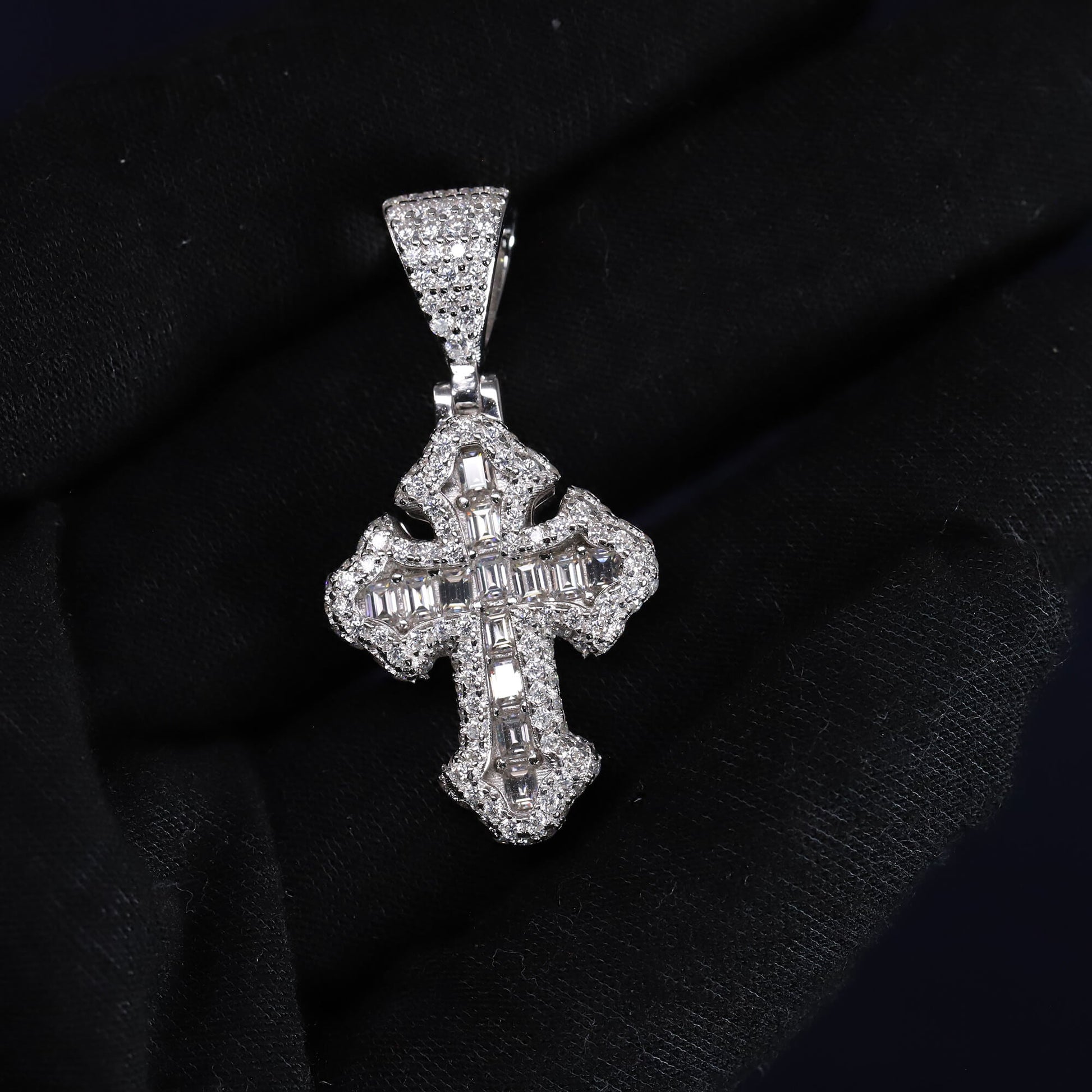 Silver cross pendant with gemstones on a black fabric background