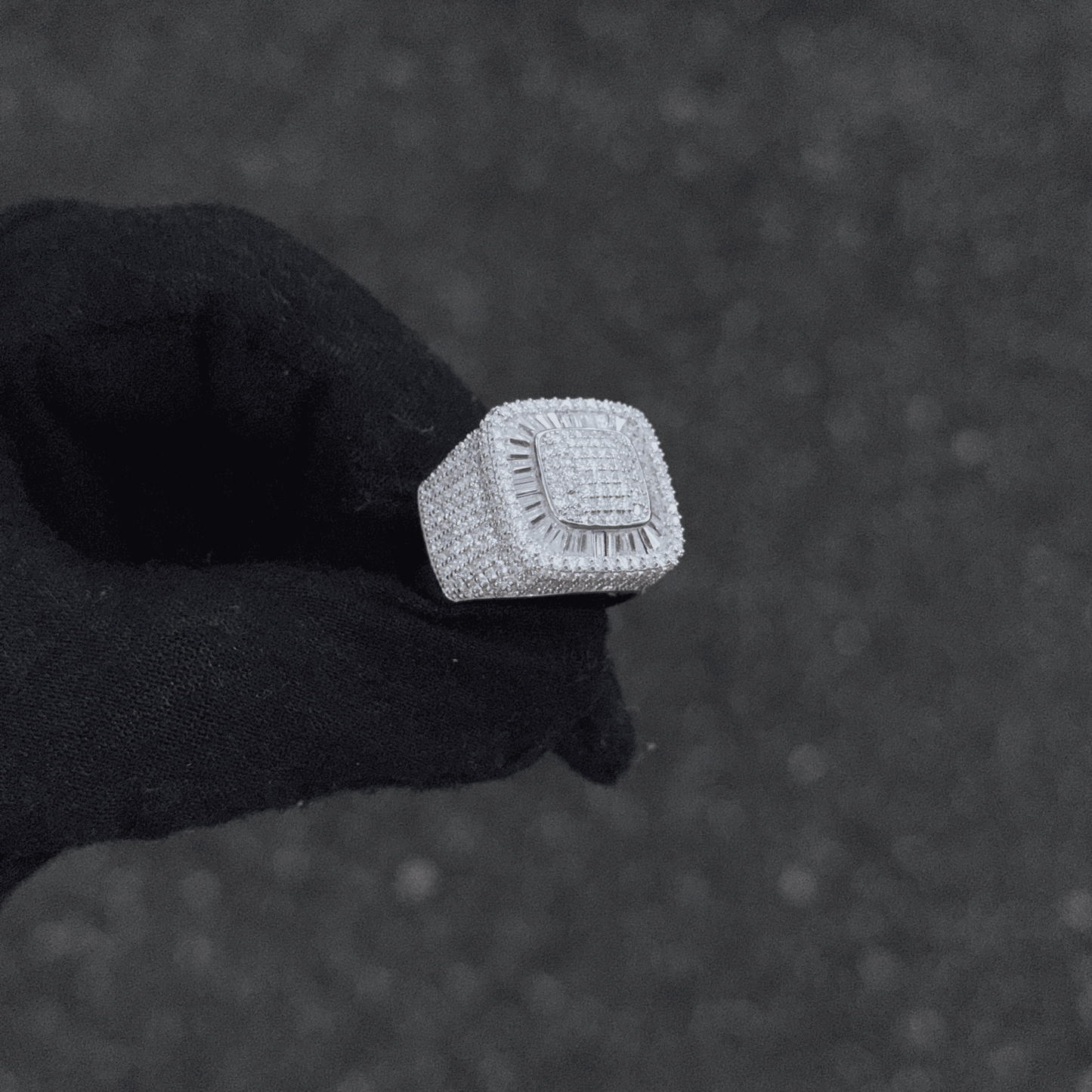 Silver ring with a textured band held by a black gloved hand against a dark background