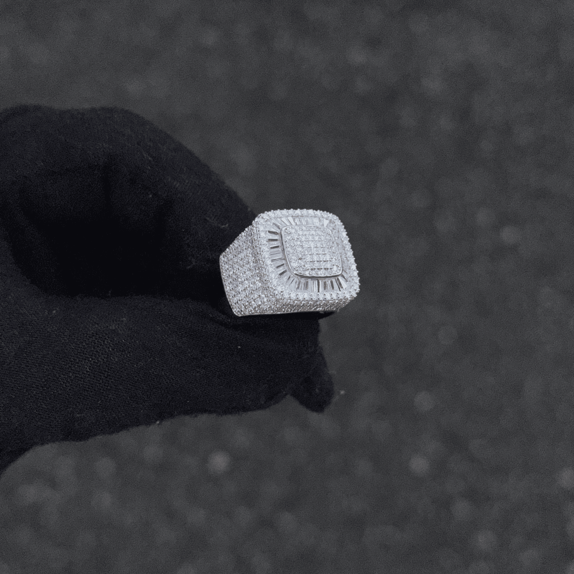 Silver ring with a textured band held by a black gloved hand against a dark background
