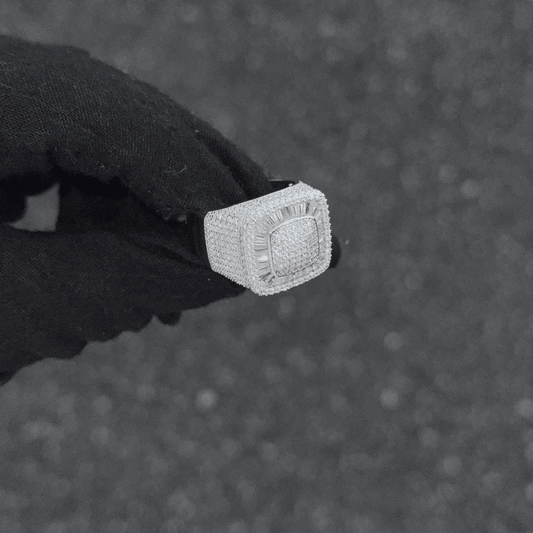 Silver ring with diamonds held by a gloved hand on a textured gray background