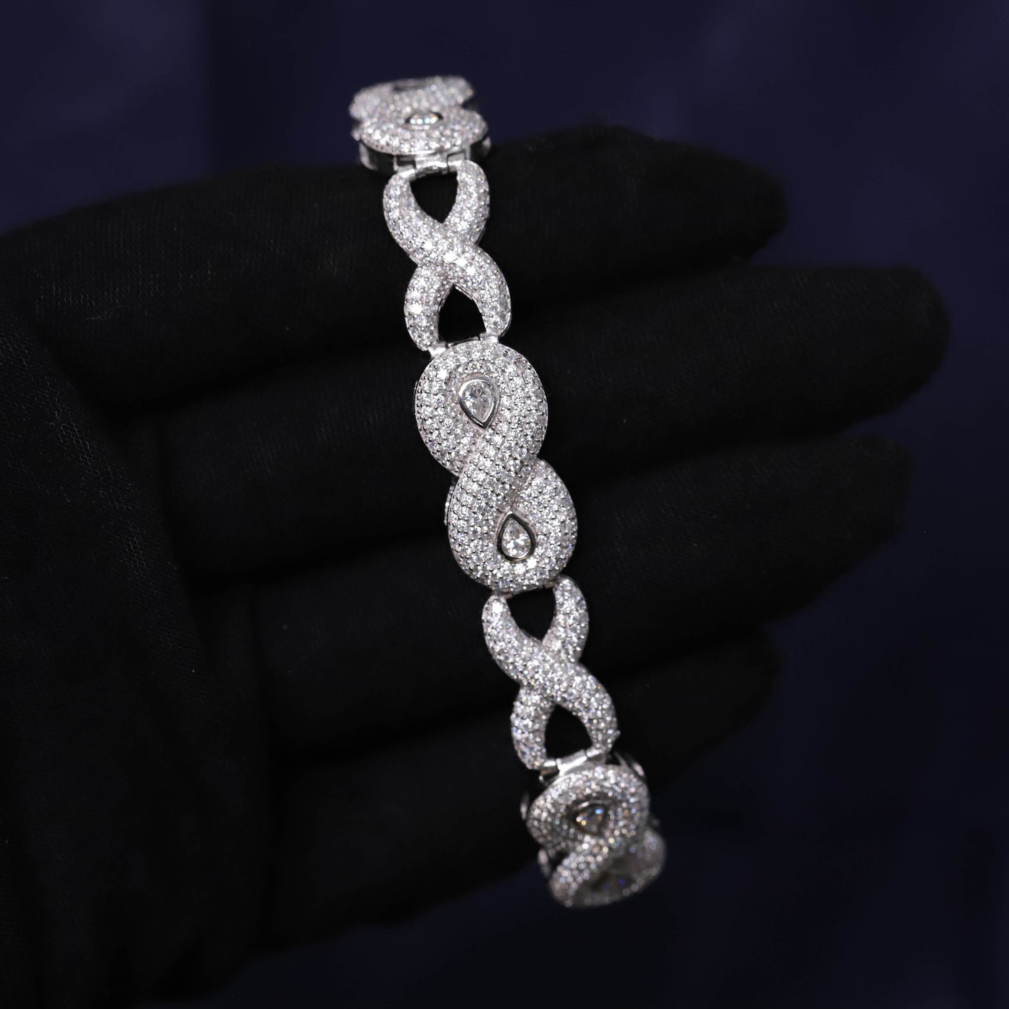 Silver bracelet with intricate design held by a gloved hand against a dark background