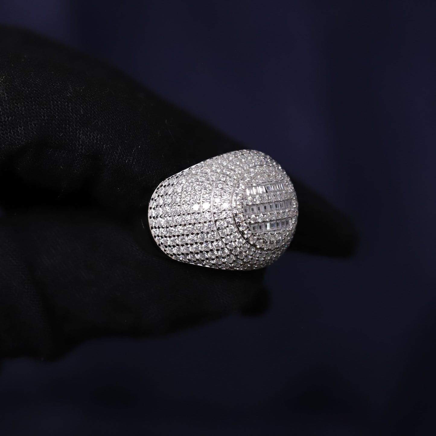 Silver ring with diamonds held by a gloved hand against a dark background