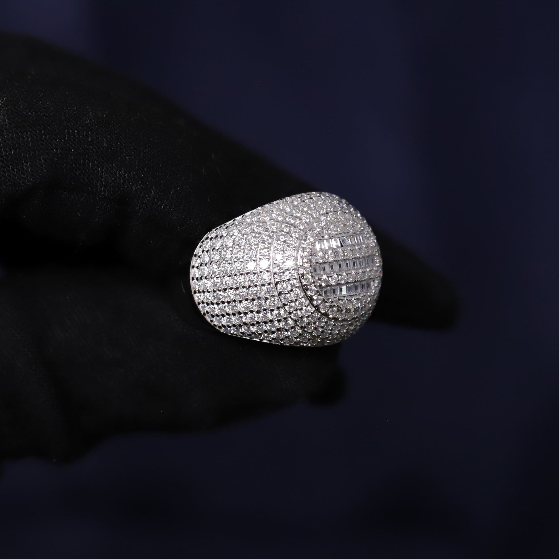Silver ring with diamonds held by a gloved hand against a dark background