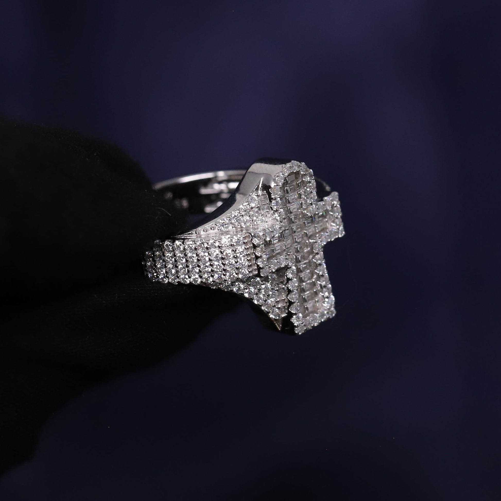 Silver cross-shaped ring with embedded stones on a dark background