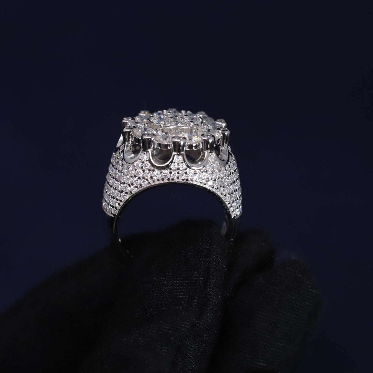 Silver ring with multiple diamonds held by a black gloved hand against a dark background