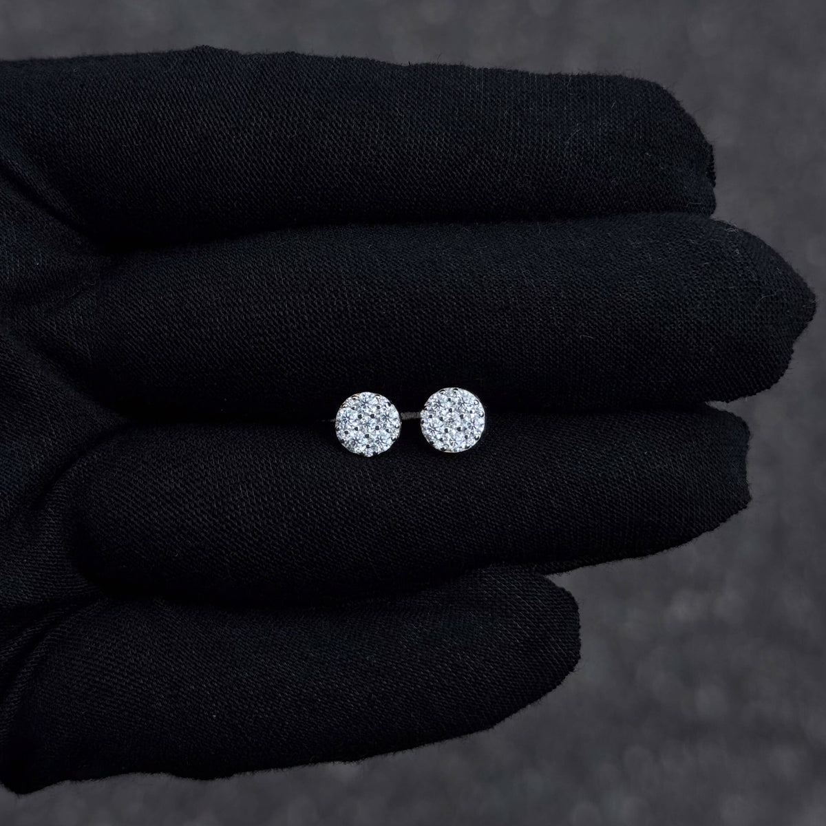 Small round sterling silver moissanite cluster stud earrings with 0.58ct diamonds shown on black glove.