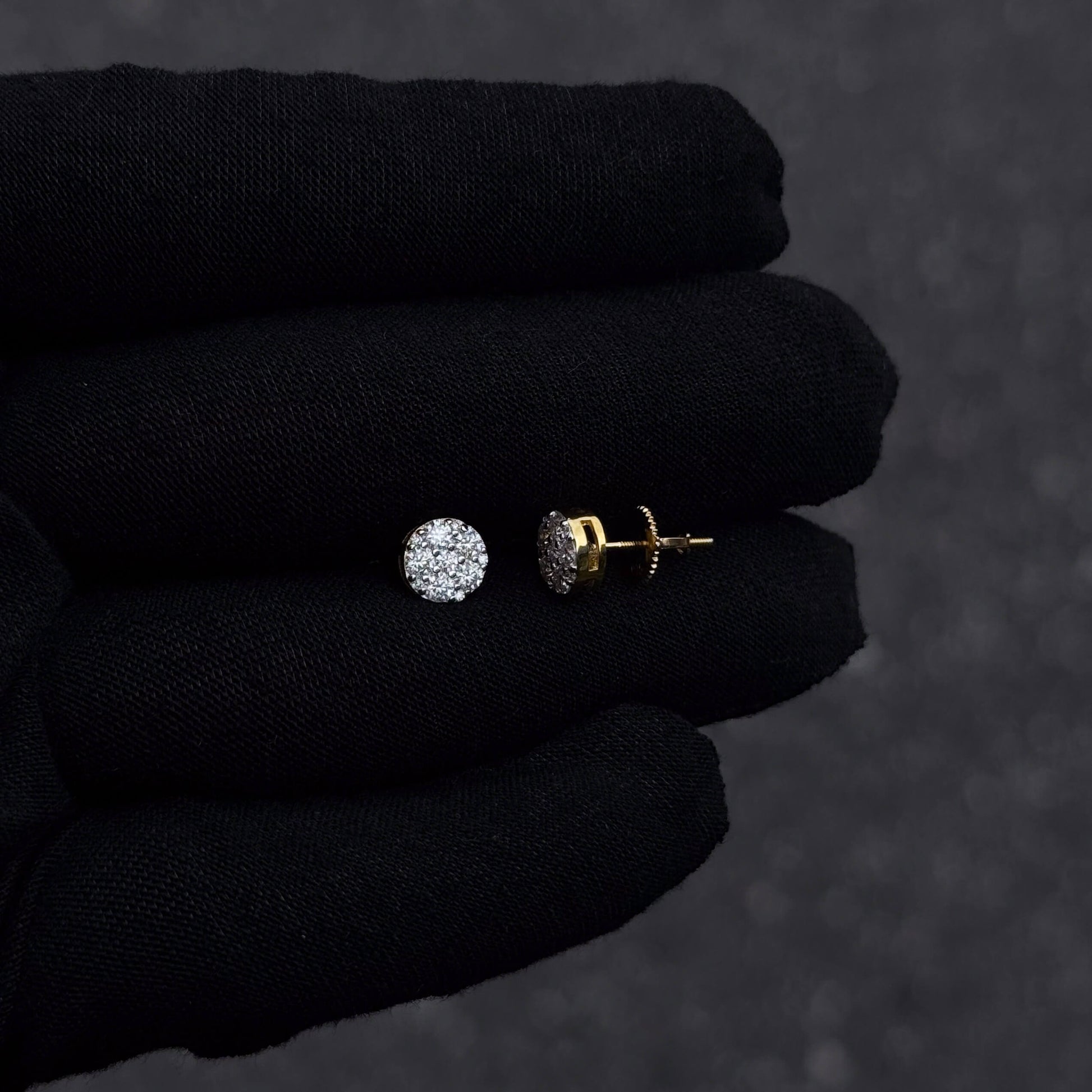 Gold-plated 7mm round moissanite cluster diamond stud earrings with screw backs shown on black glove.