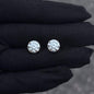 Pair of round moissanite solitaire stud earrings in sterling silver displayed on black glove.