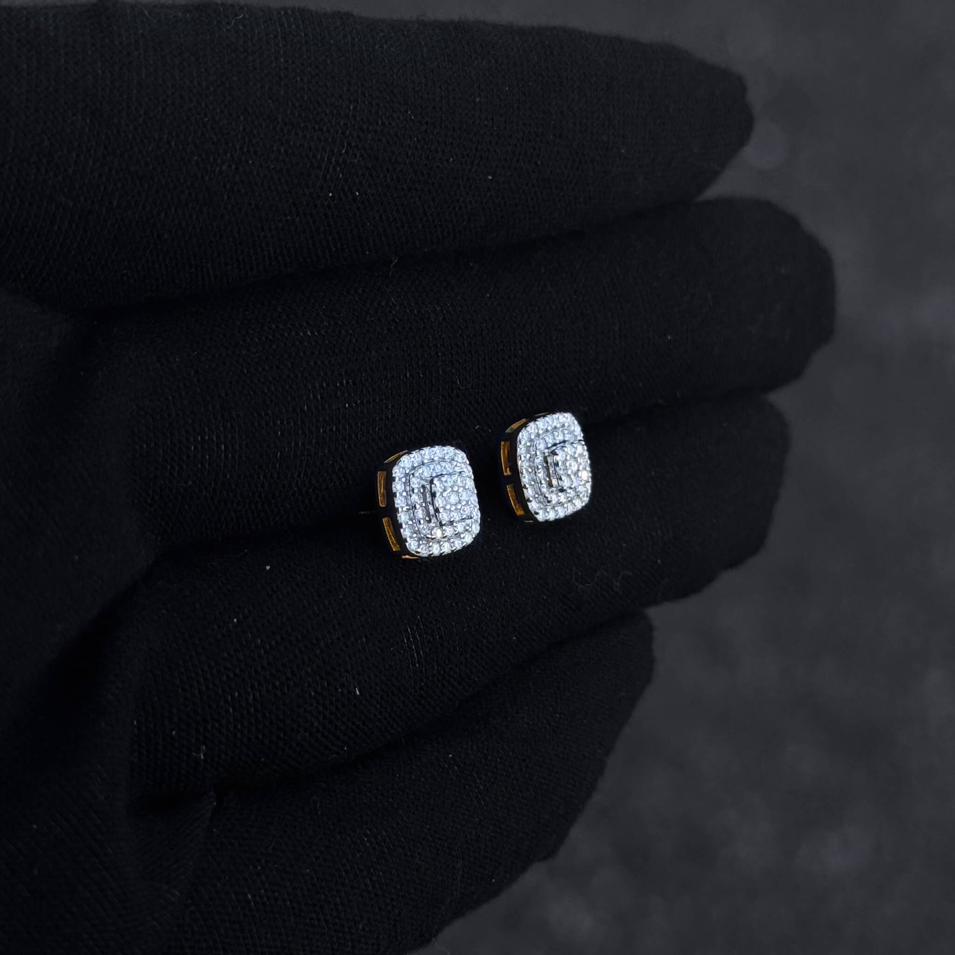Gold-trim square moissanite cluster earrings shown on black glove, featuring triple halo diamond detail.