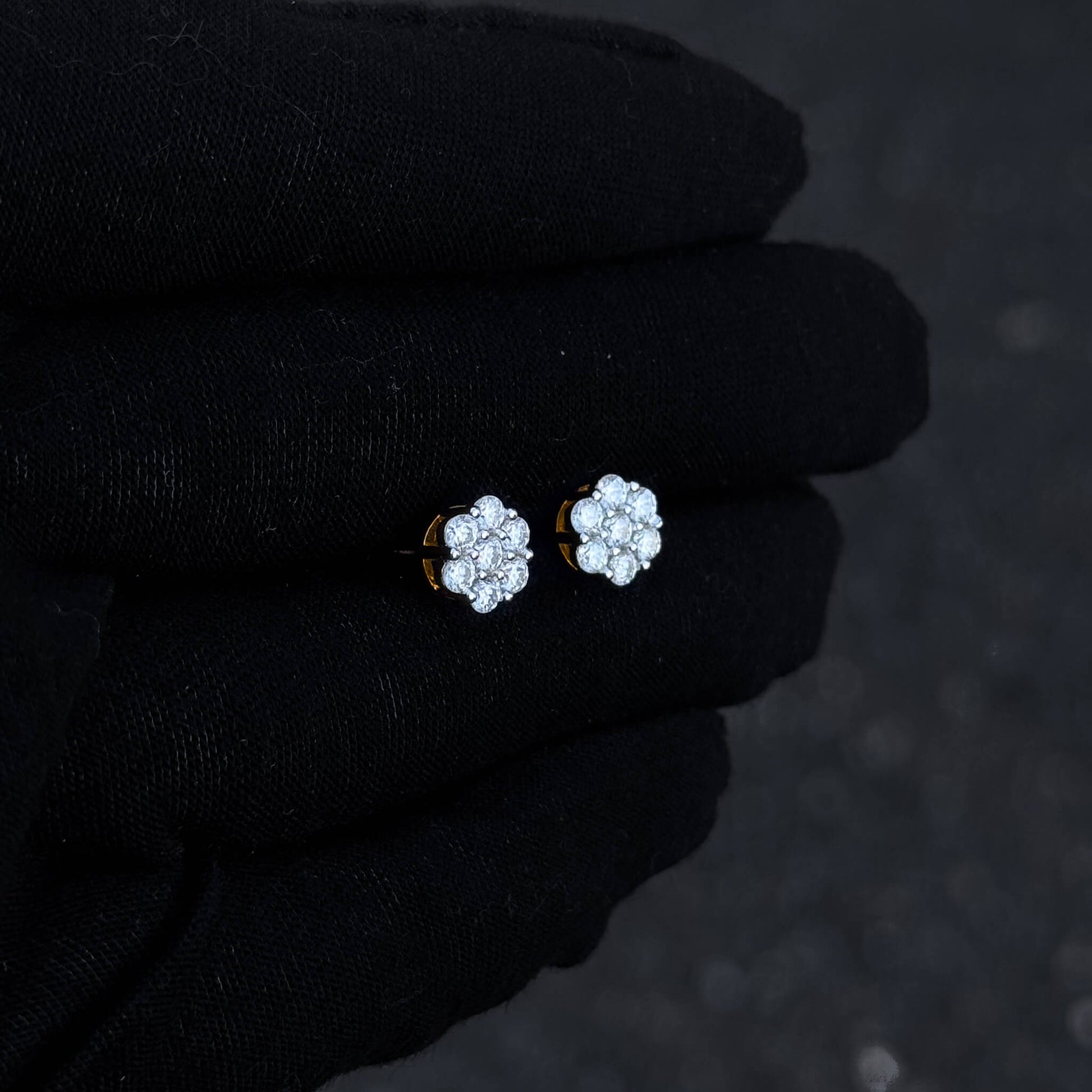 Small floral moissanite cluster earrings shown on black glove with warm silver detailing.