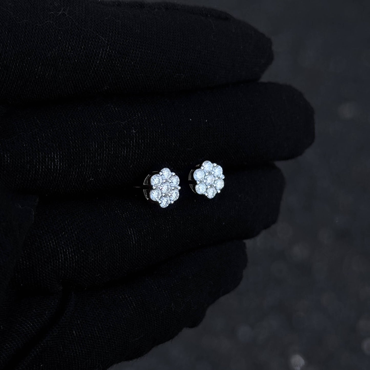 Sterling silver 8mm moissanite floral stud earrings displayed on black glove in low light.