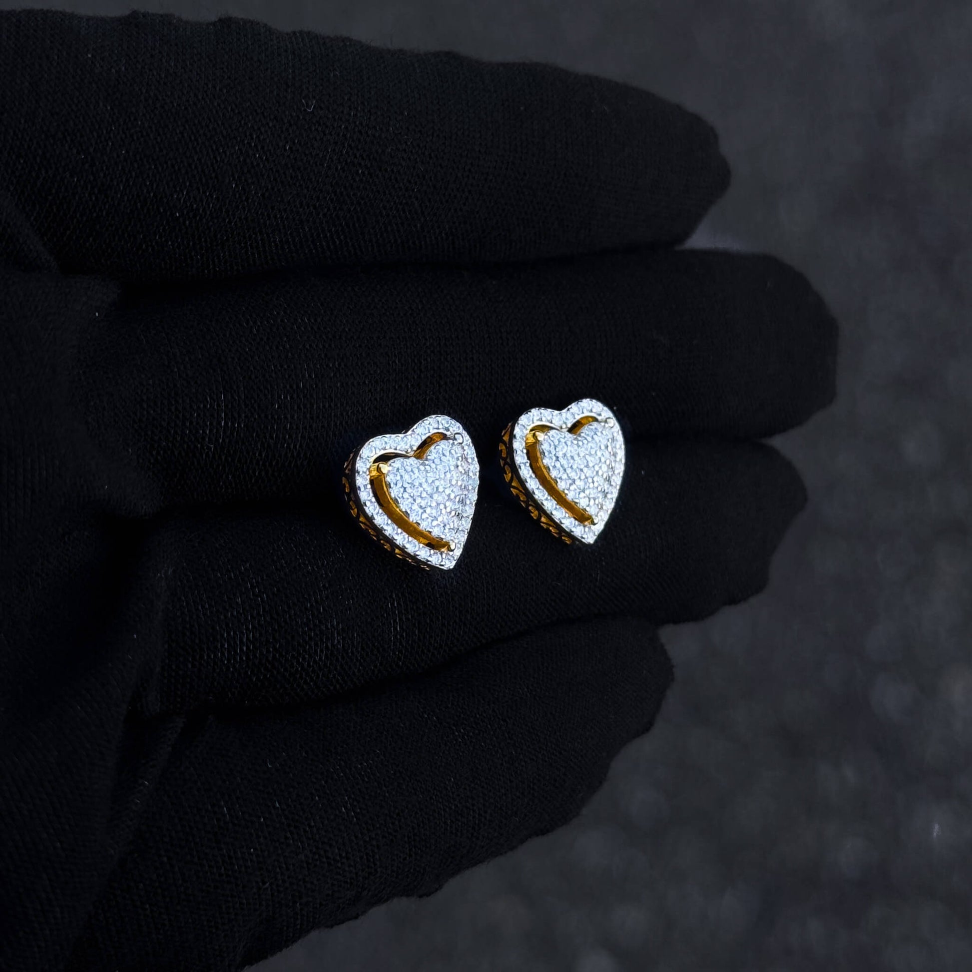 Gold heart moissanite cluster stud earrings shown on black glove with pavé detailing.