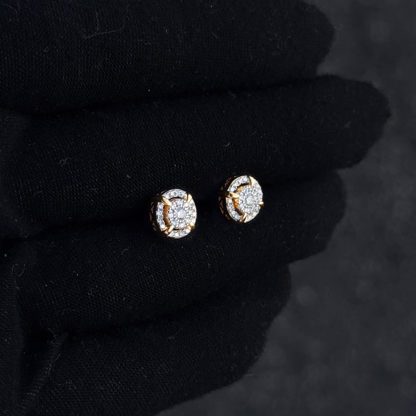 Gold halo moissanite cluster stud earrings shown on black glove with round diamond pavé accents.