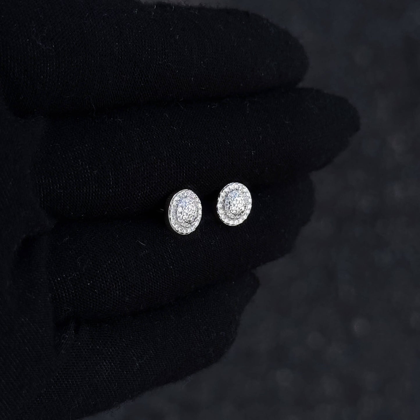 Round Moissanite cluster earrings in sterling silver displayed on black glove for scale.