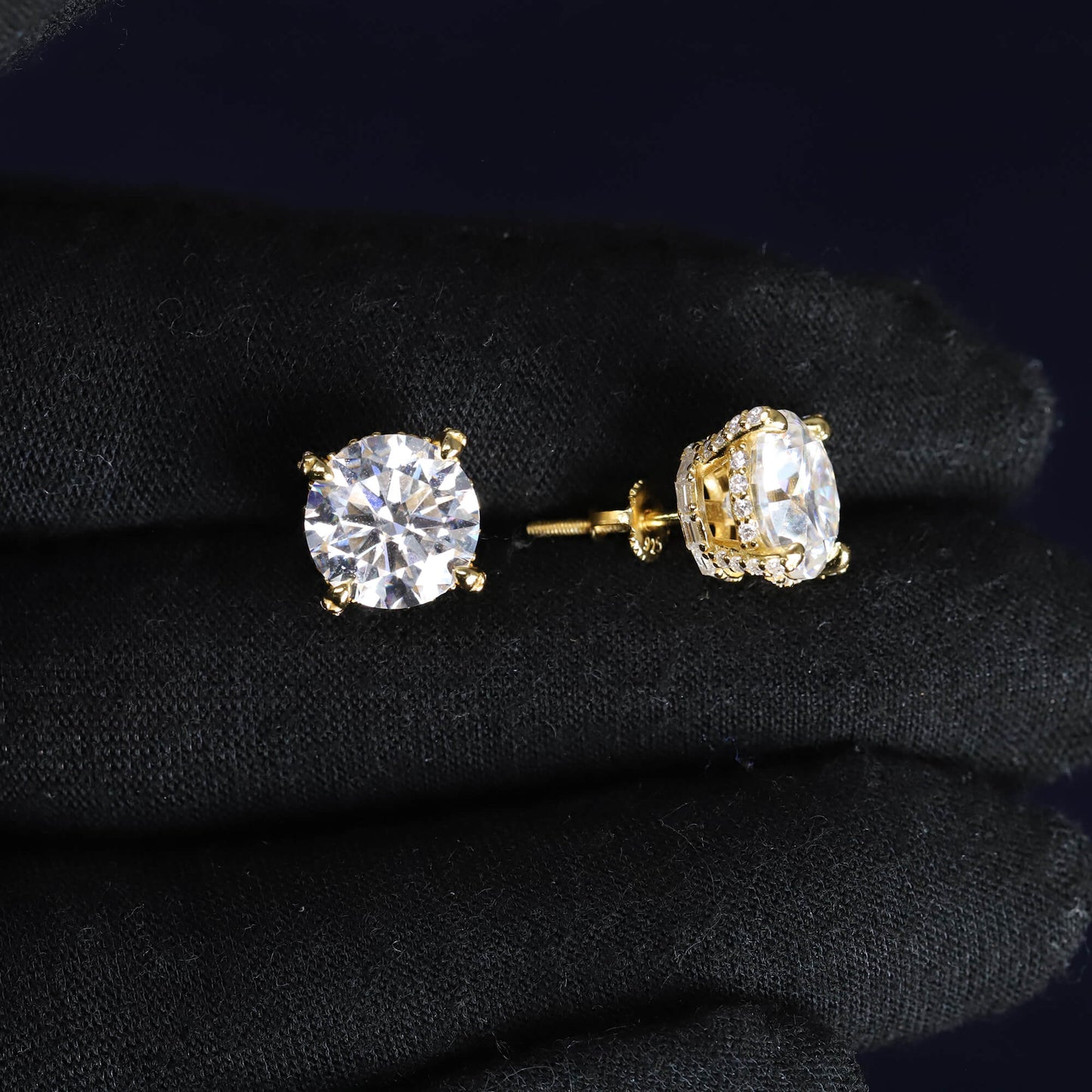 Gold stud earrings with clear gemstones on a black fabric background