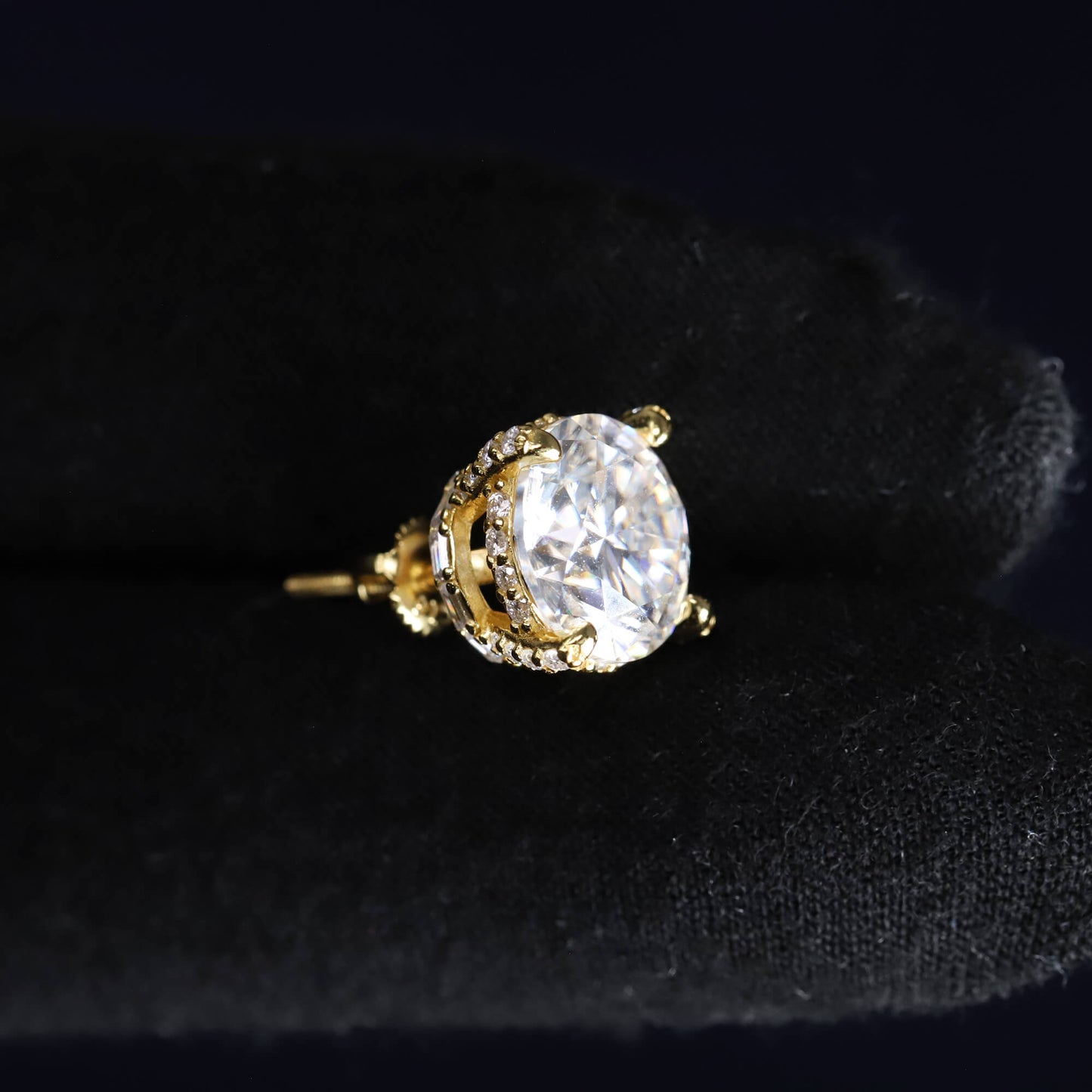 Gold earring with a large clear gemstone on a black background