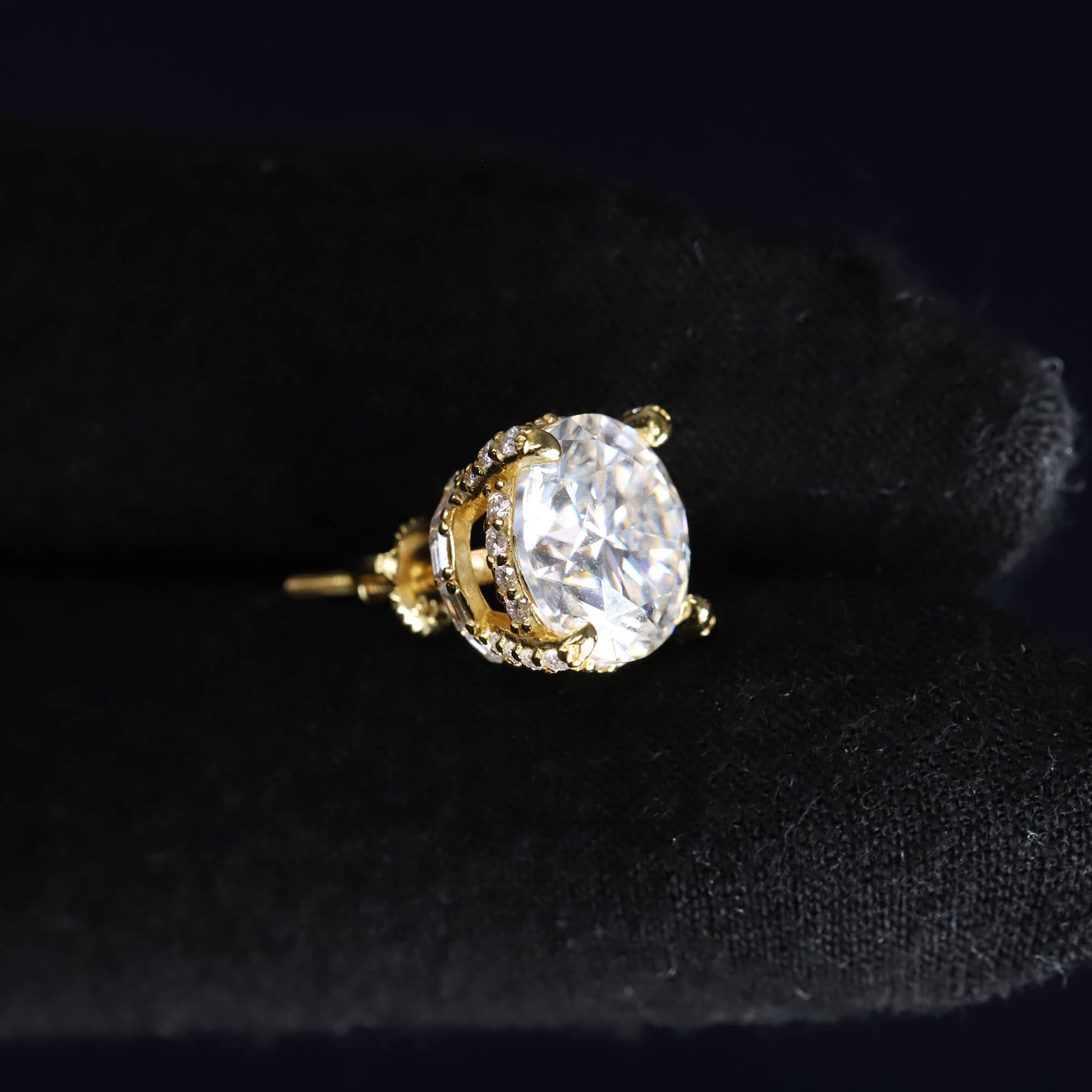 Gold earring with a large clear gemstone on a black background