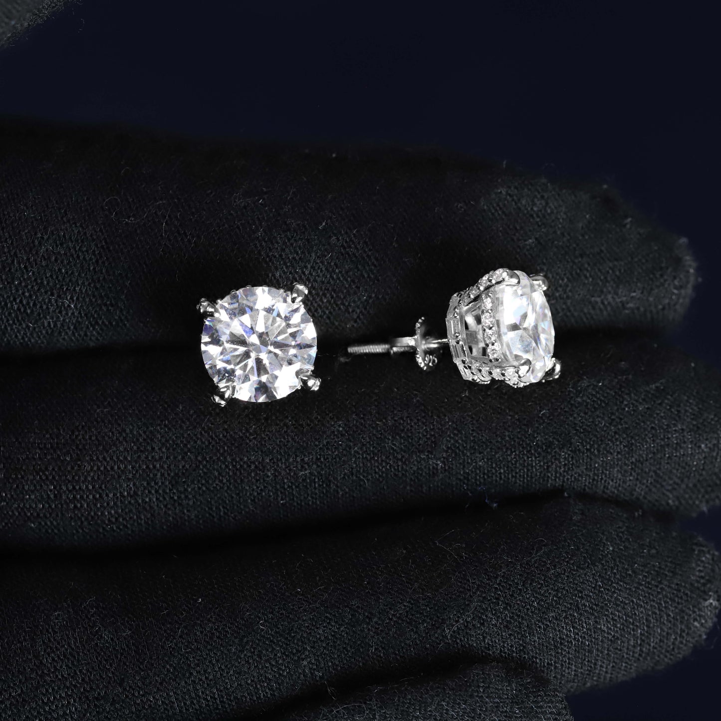 Pair of diamond stud earrings on a dark fabric background