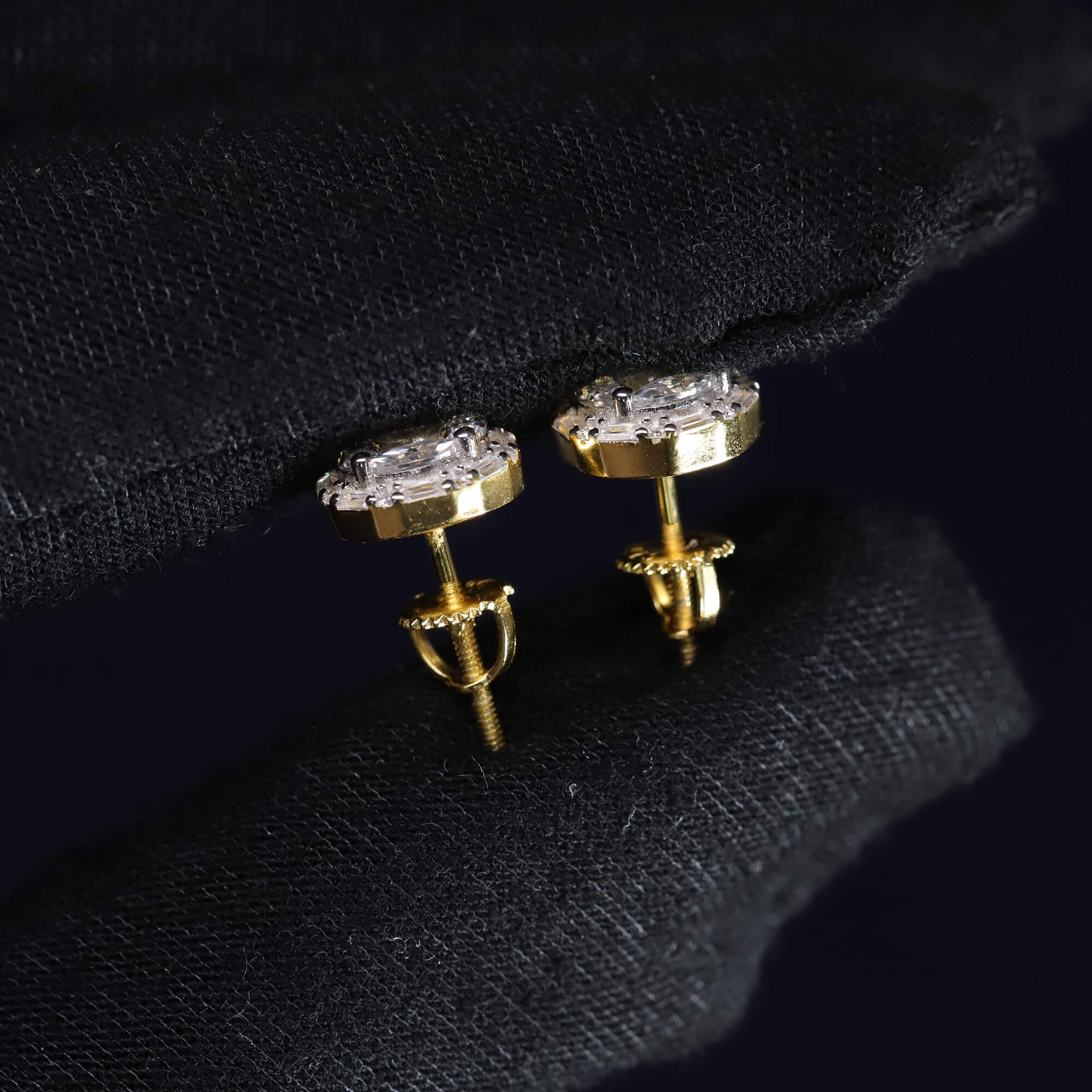 Gold earrings with clear gemstones on a black fabric background