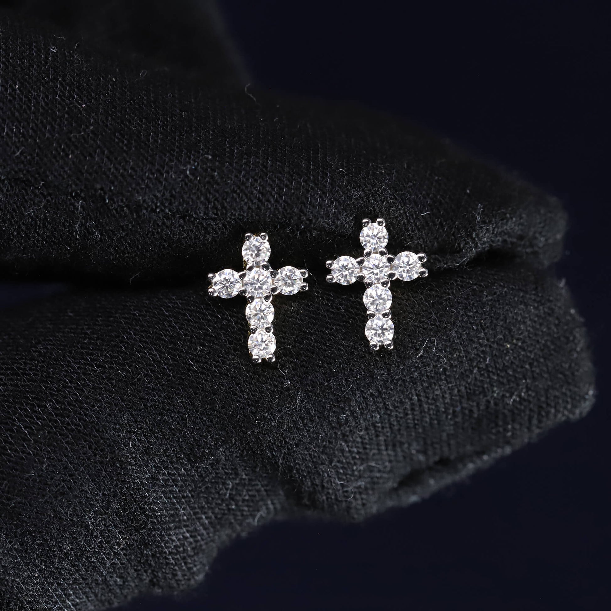 Pair of diamond cross earrings on a black fabric background