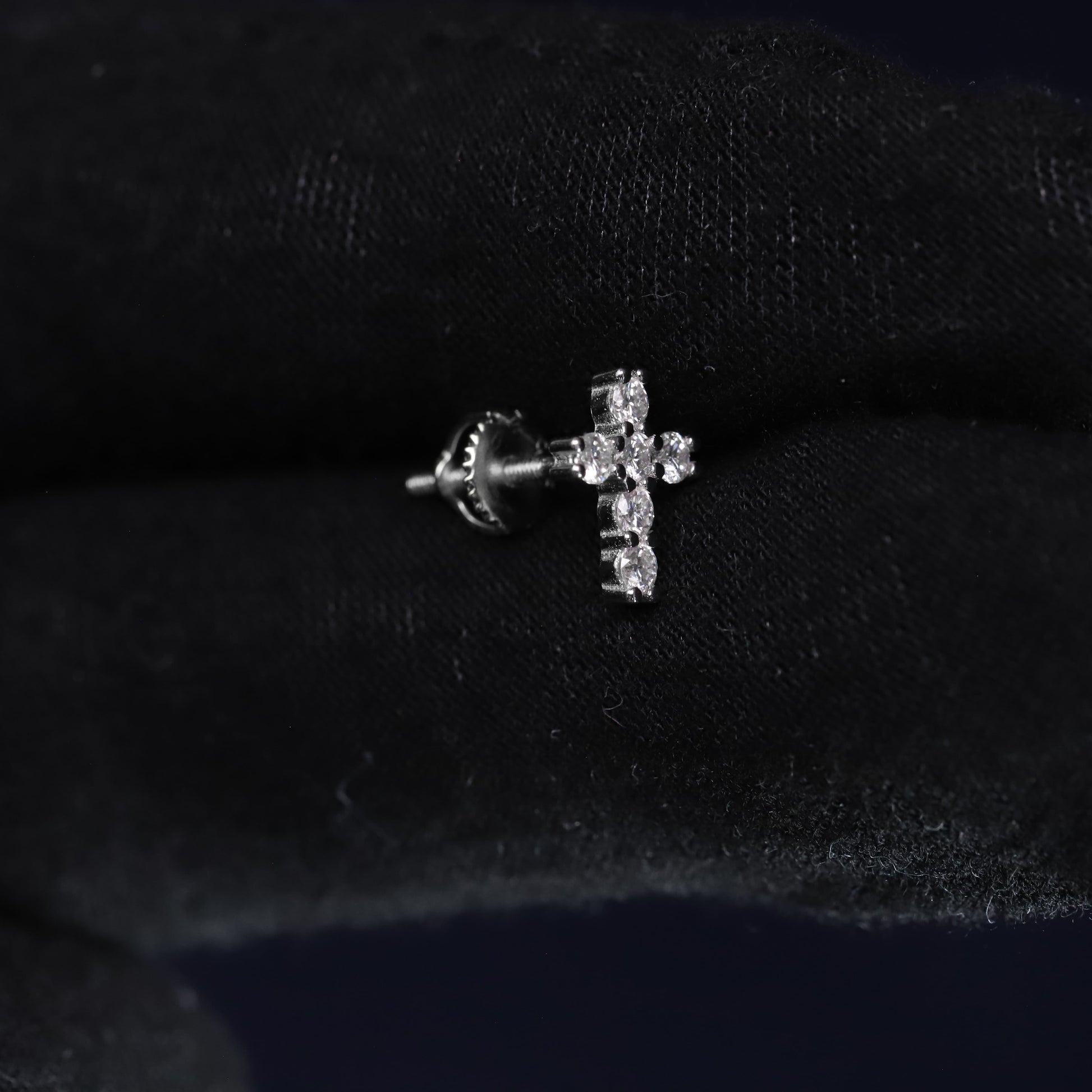 Silver cross-shaped earring on a black fabric background