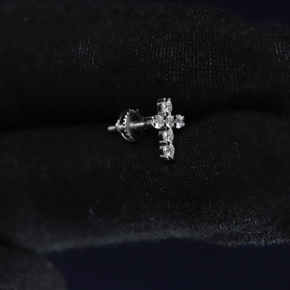 Silver cross-shaped earring on a black fabric background