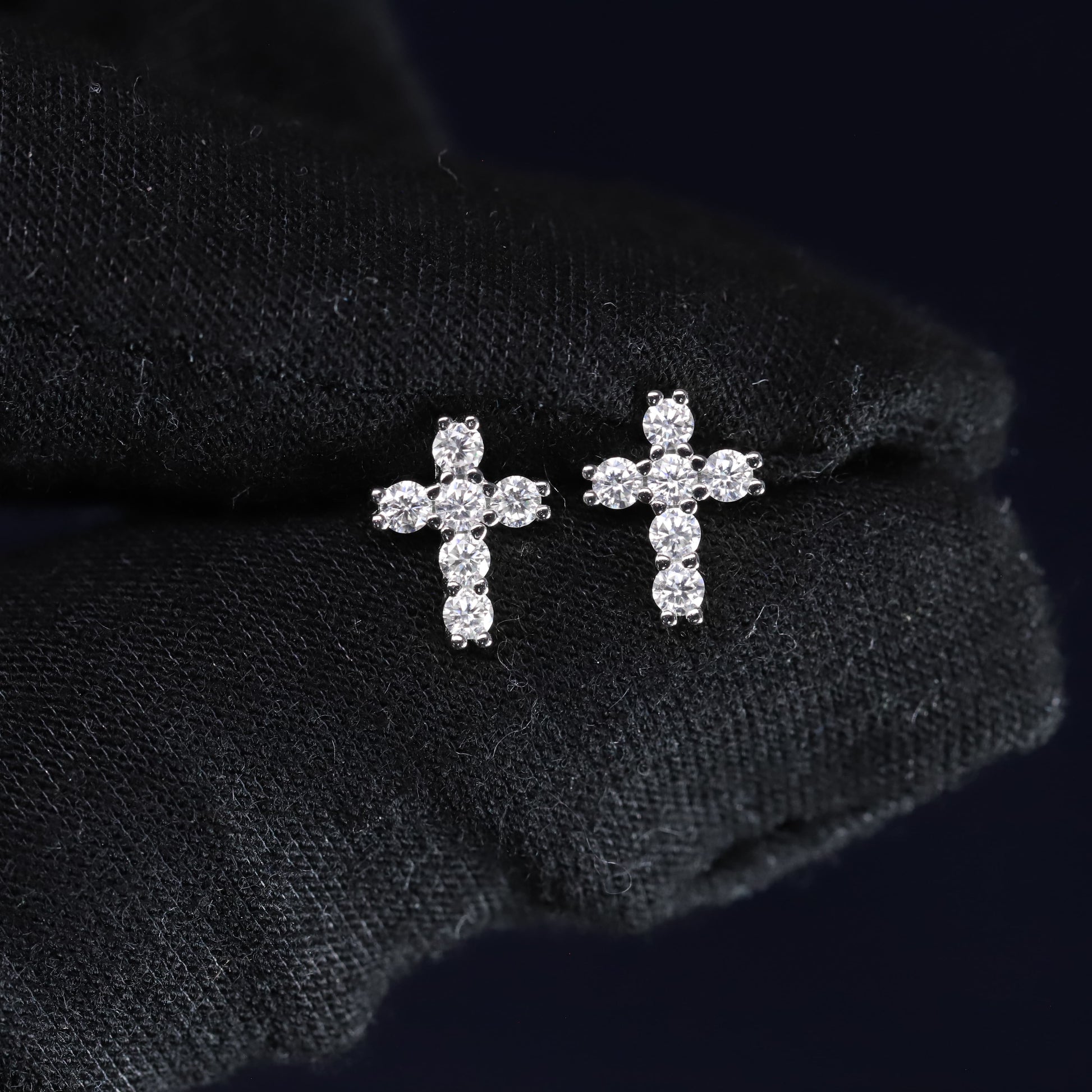 Pair of diamond cross earrings on a black fabric background