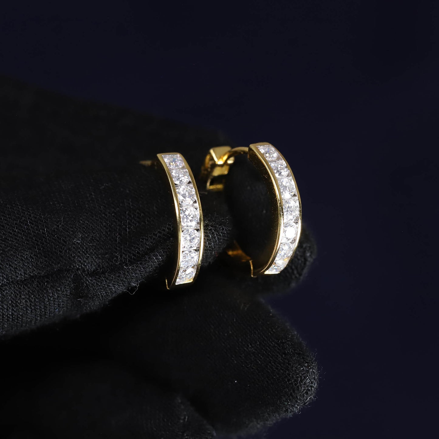 Gold hoop earrings with clear stones on a black surface