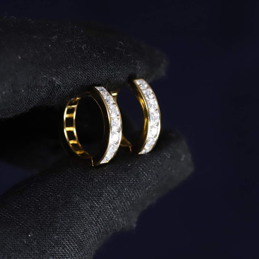 Gold hoop earrings with embedded diamonds on a dark fabric background
