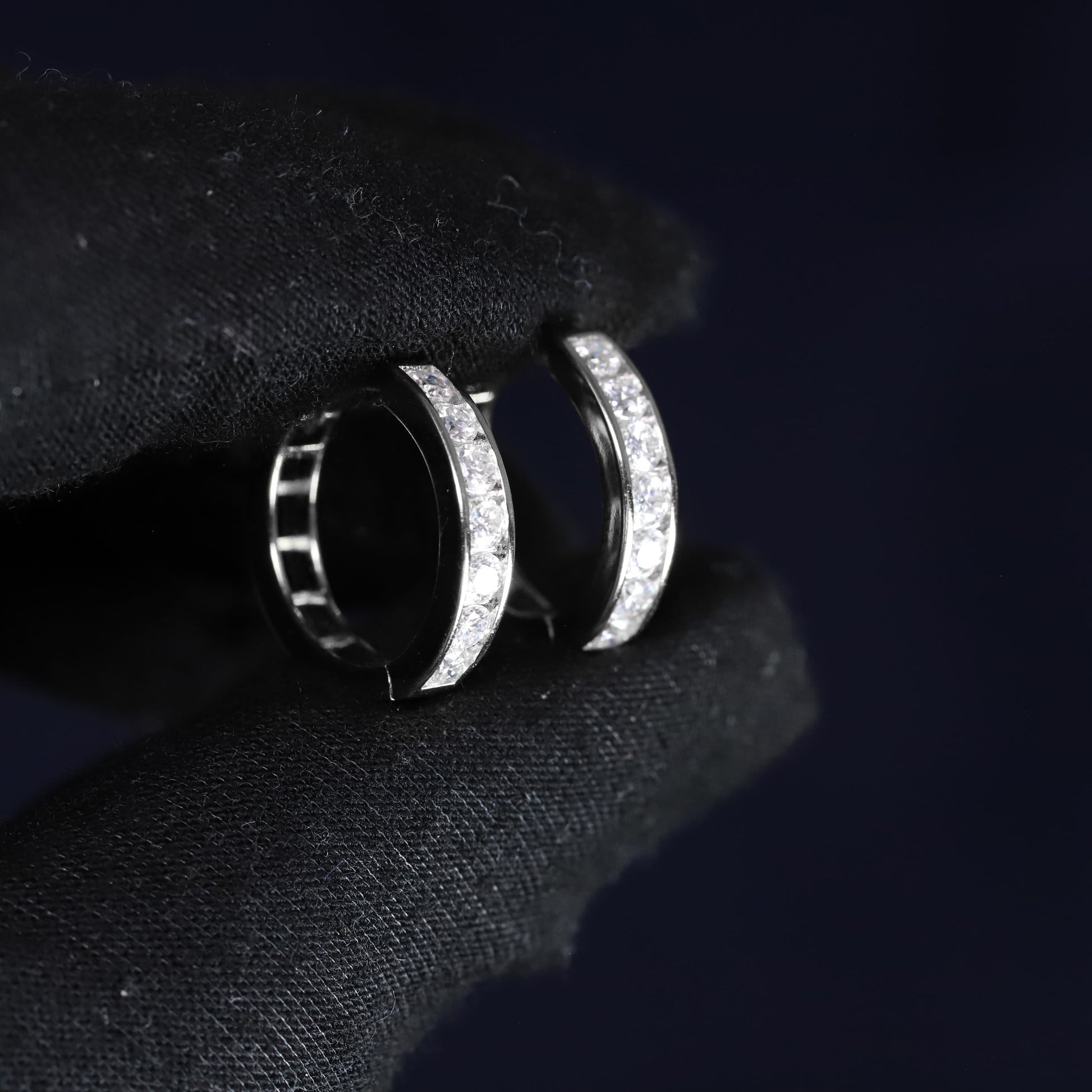 Silver hoop earrings with embedded stones on a black fabric background