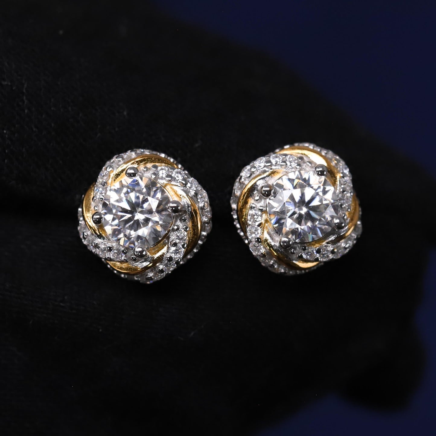 Pair of gold and silver earrings with clear gemstones on a dark background