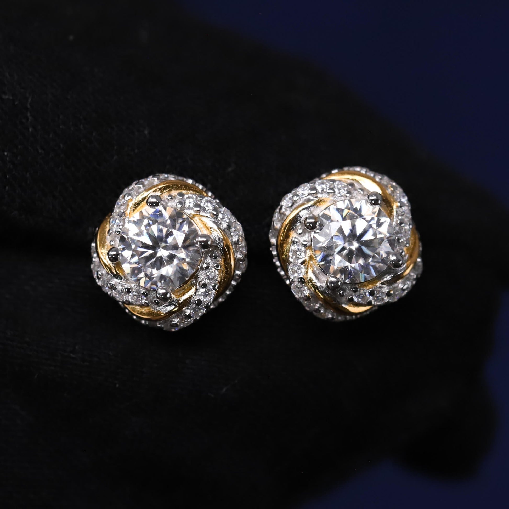 Pair of gold and silver earrings with clear gemstones on a dark background