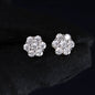 Pair of silver flower-shaped earrings with clear stones on a black background