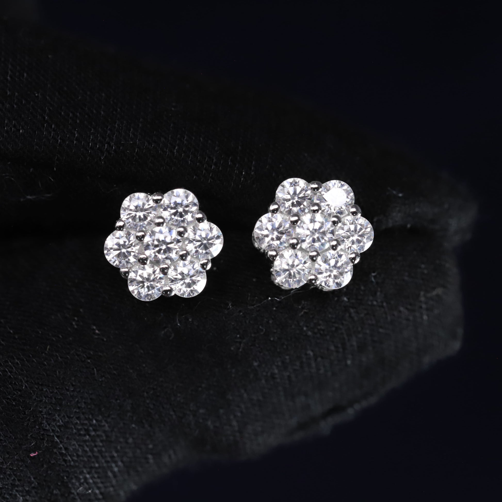 Pair of silver flower-shaped earrings with clear stones on a black background