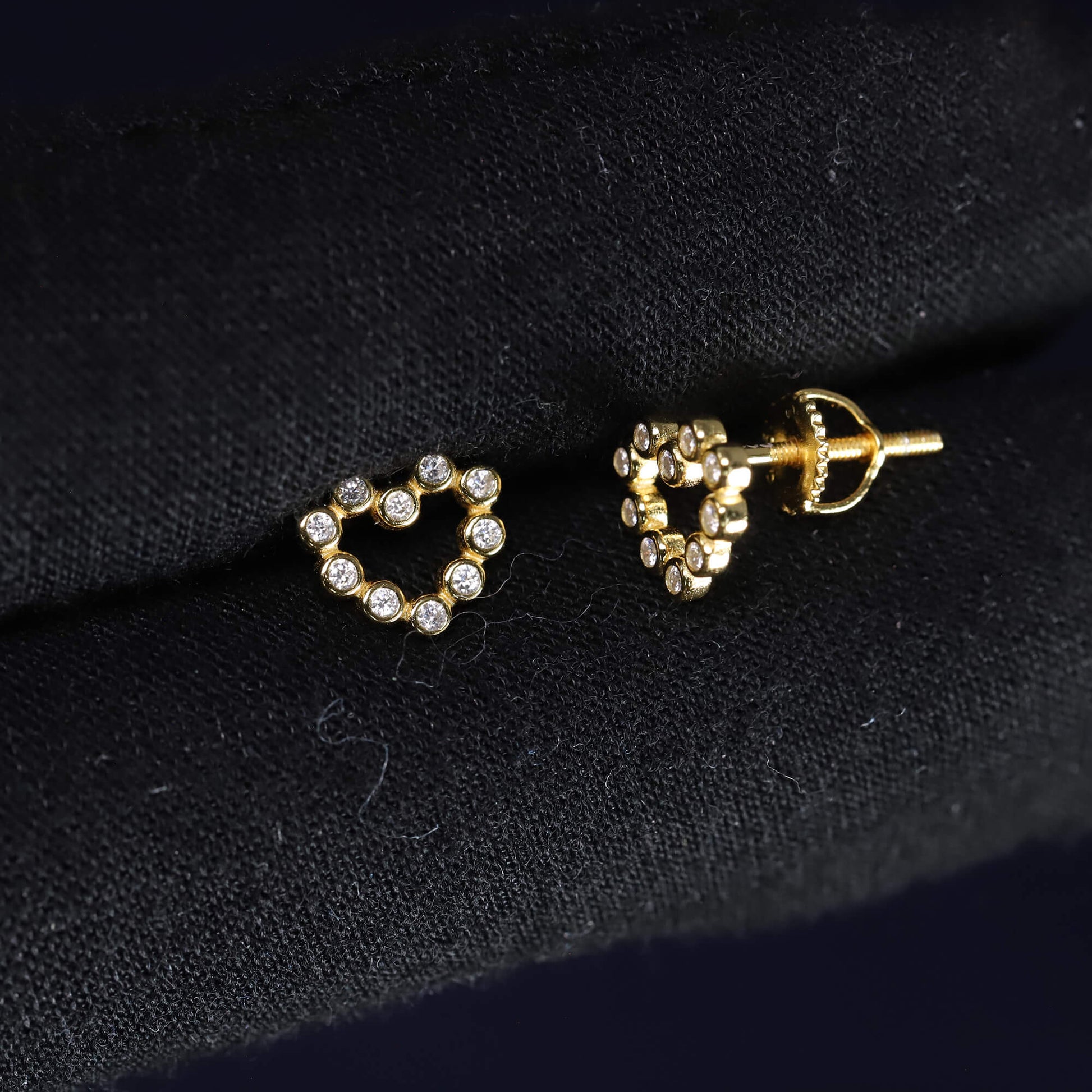 Heart-shaped earrings with gold and clear stones on a dark fabric background