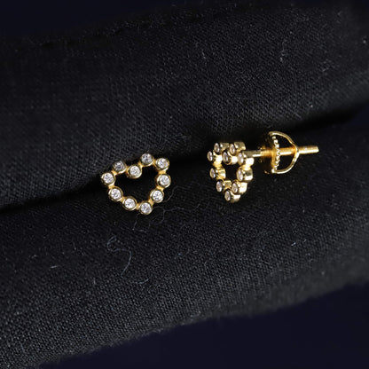 Heart-shaped earrings with gold and clear stones on a dark fabric background