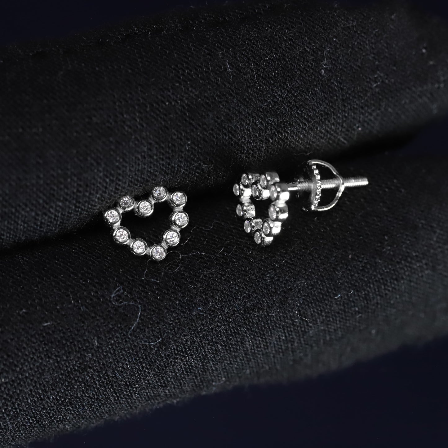 Heart-shaped silver earrings with clear stones on a black fabric background