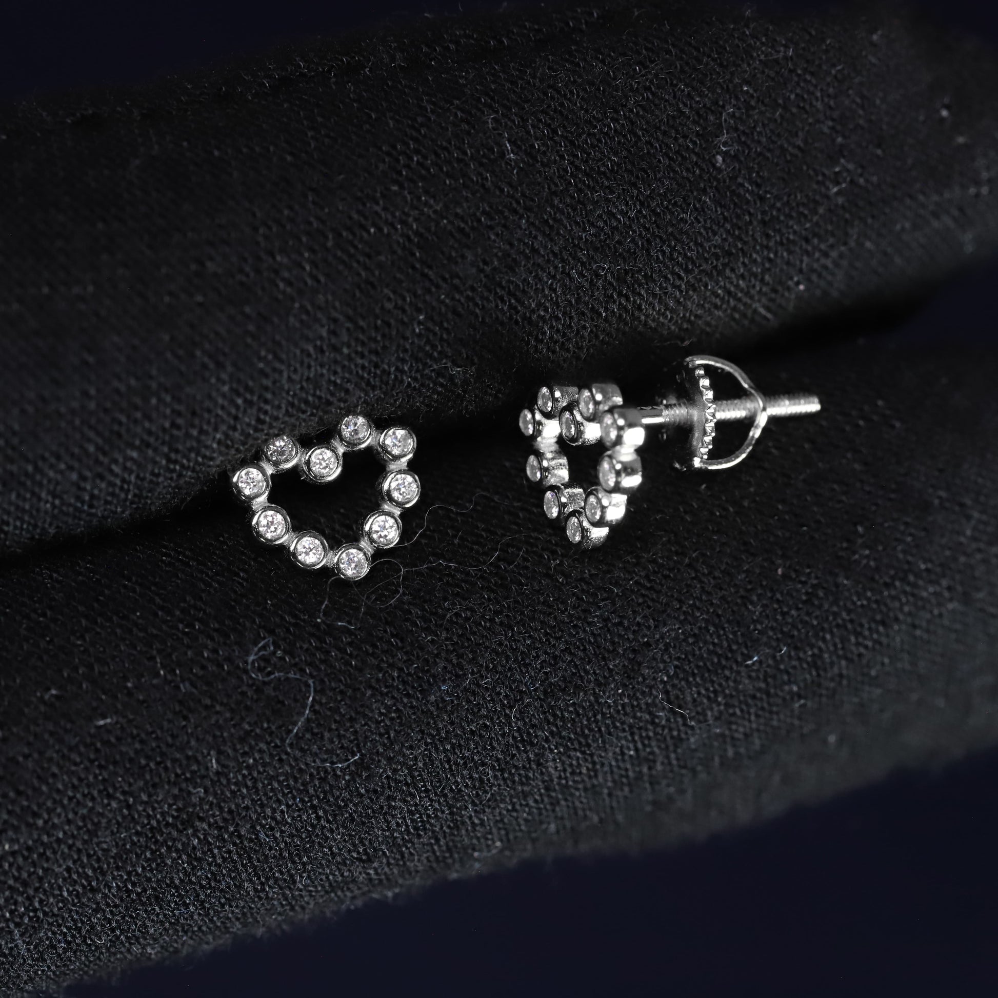 Heart-shaped silver earrings with clear stones on a black fabric background
