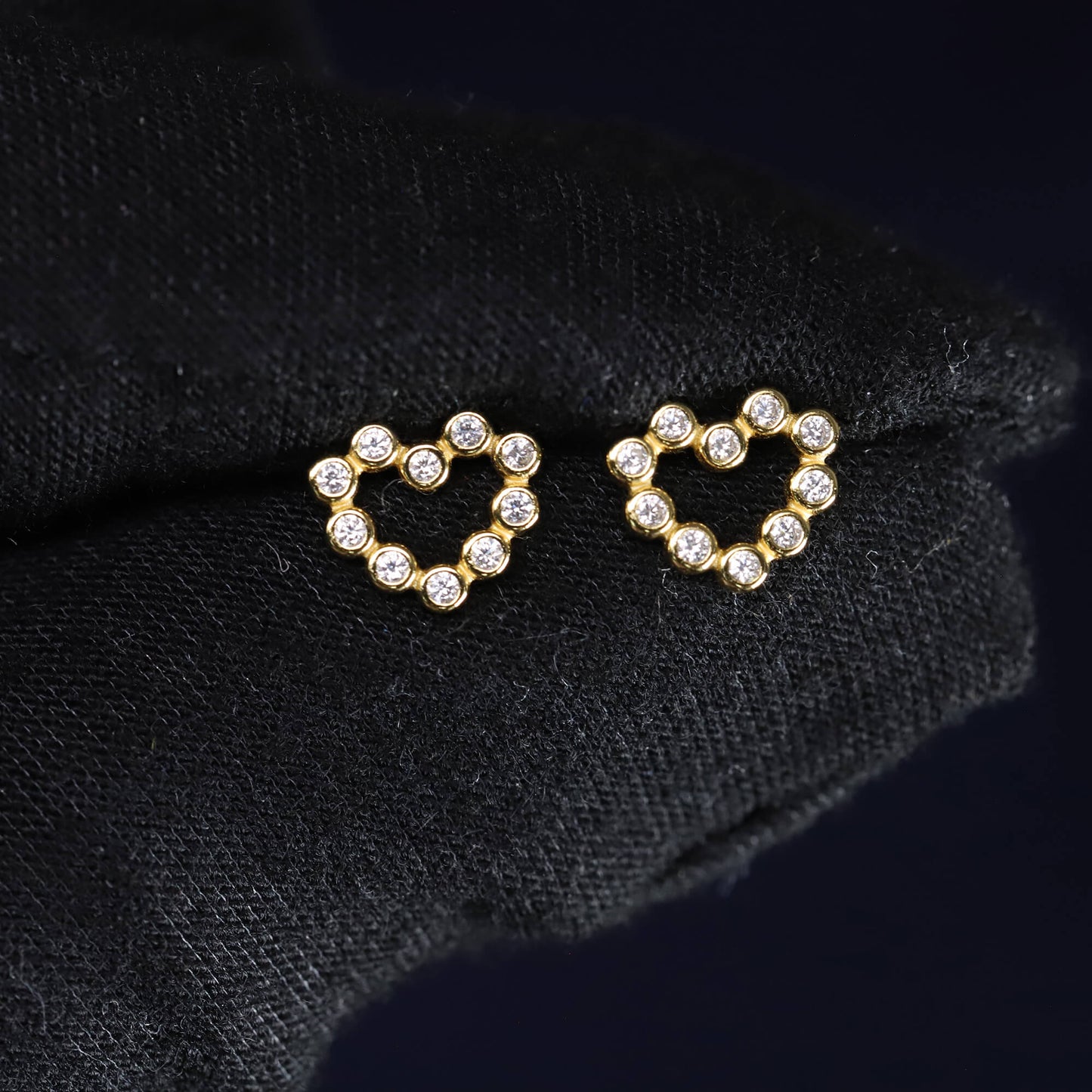 Heart-shaped earrings with clear stones on a black fabric background