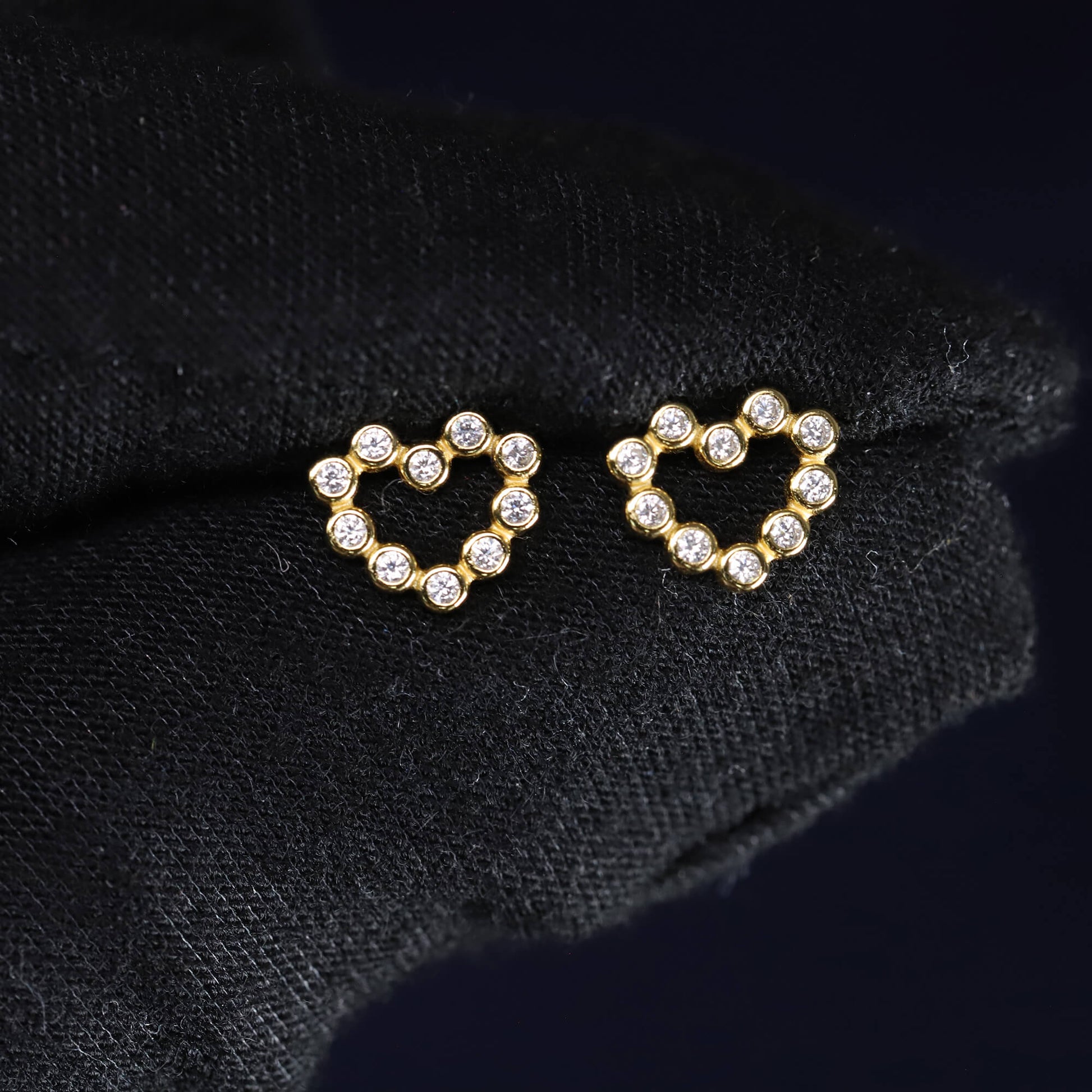 Heart-shaped earrings with clear stones on a black fabric background