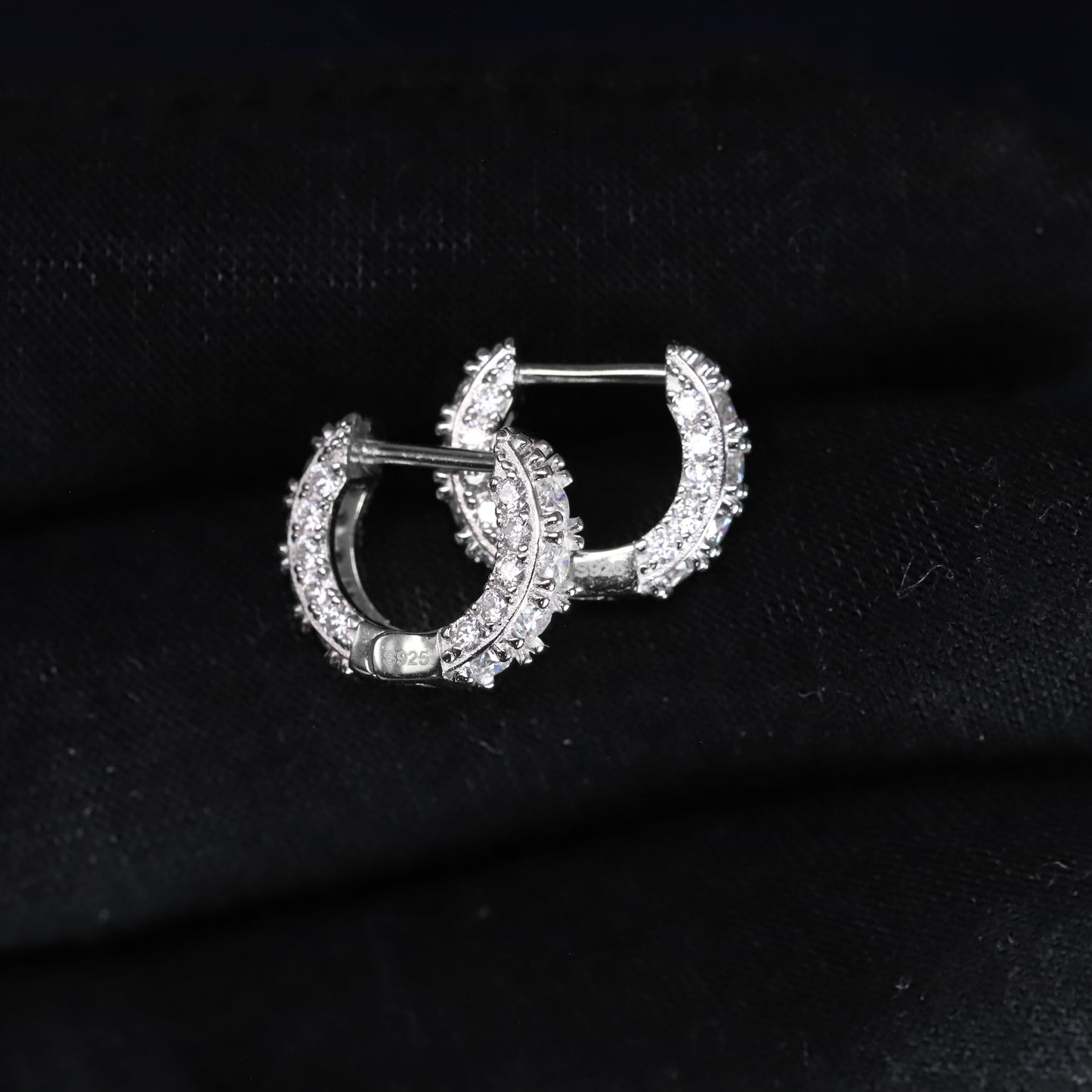 Pair of silver hoop earrings with clear stones on a black fabric background