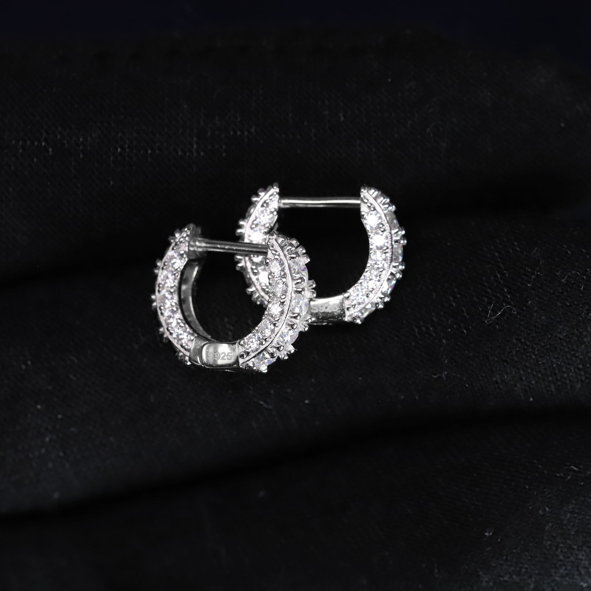 Pair of silver hoop earrings with clear stones on a black fabric background