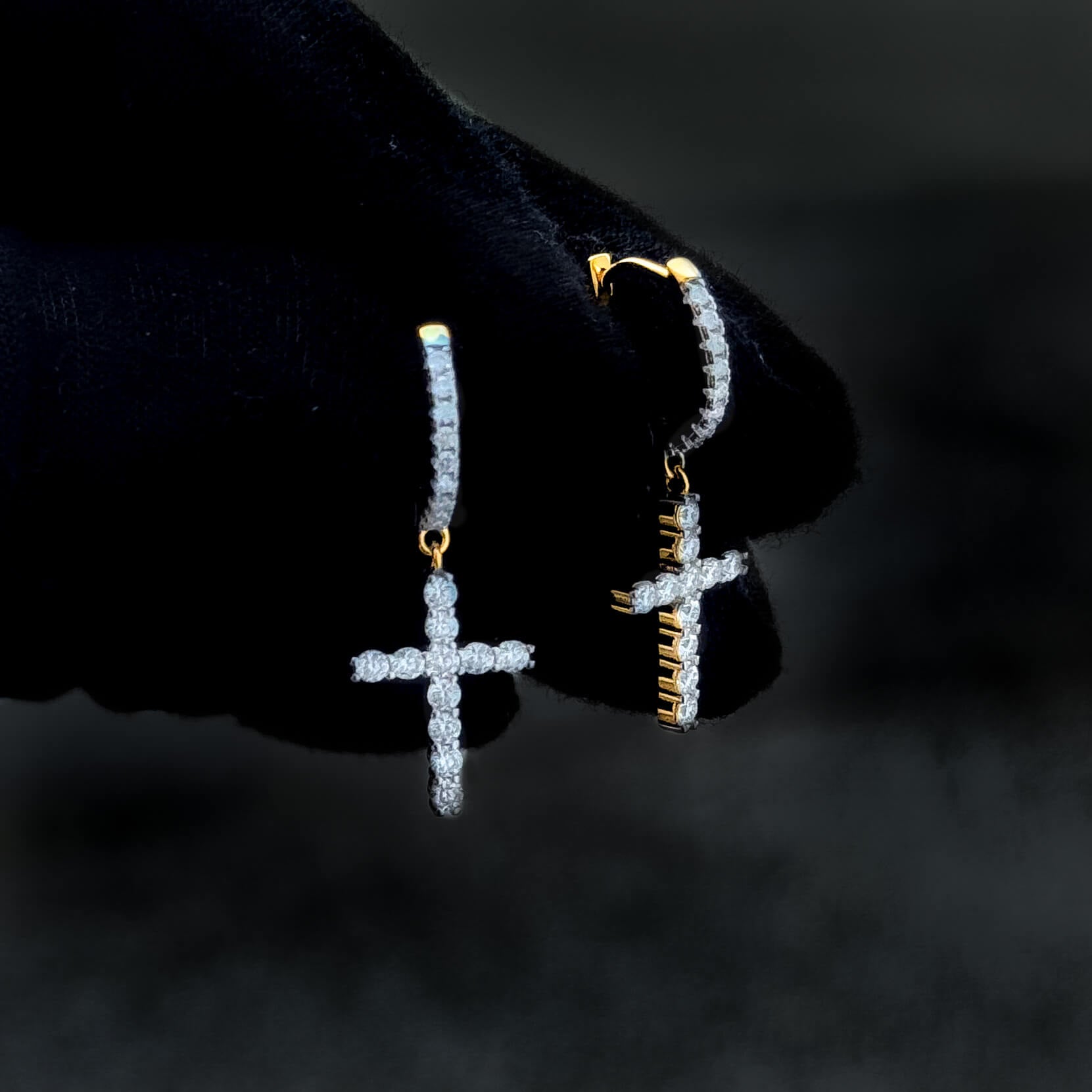 Gold-accent moissanite cross drop earrings with shimmering diamond clusters shown on glove.