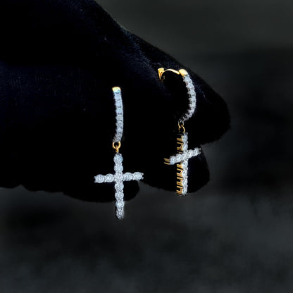 Gold-accent moissanite cross drop earrings with shimmering diamond clusters shown on glove.