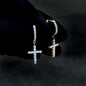 Gold-accent moissanite cross drop earrings with shimmering diamond clusters shown on glove.