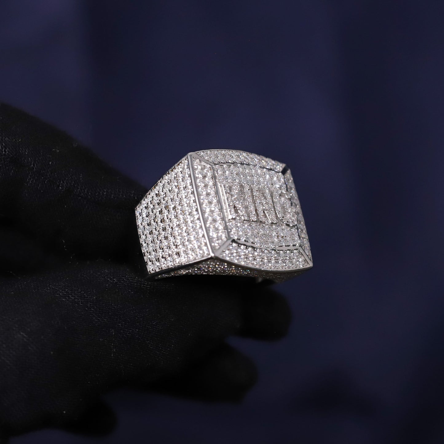 Silver ring with gemstones held by a gloved hand against a dark background